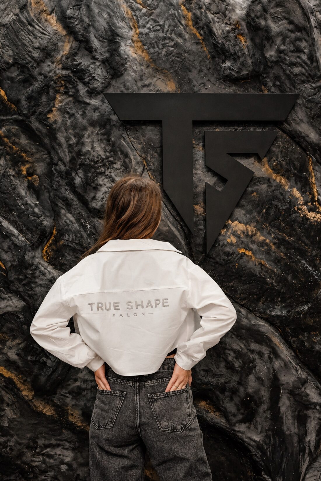 Camisa da True Shape em frente ao símbolo da marca na parede de pedra